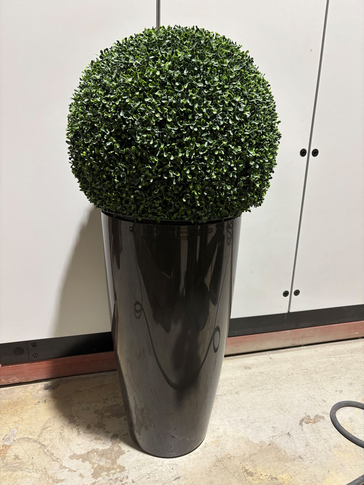 Kunstig grønn plante i mørk grå potte