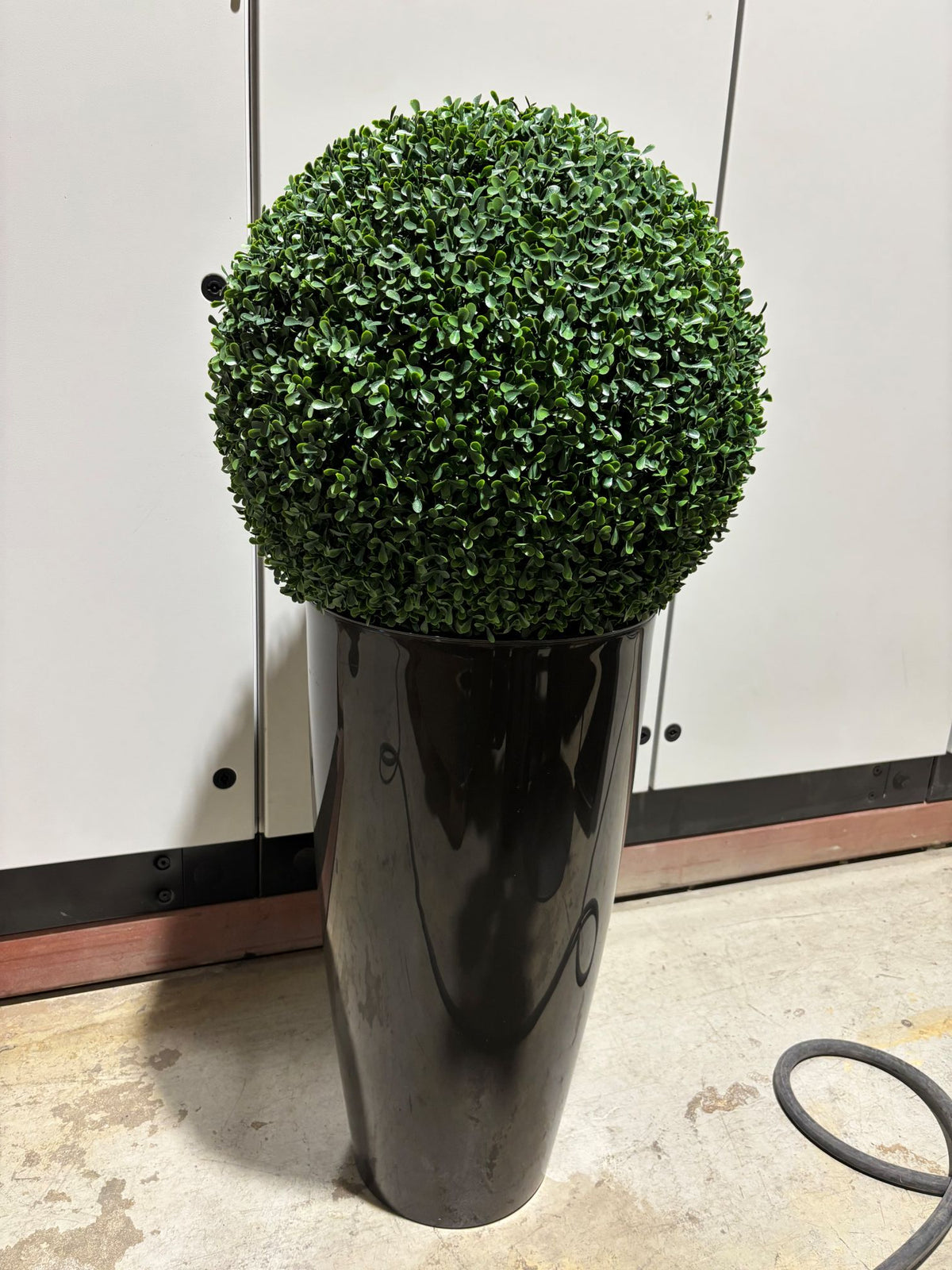 Kunstig grønn plante i mørk grå potte